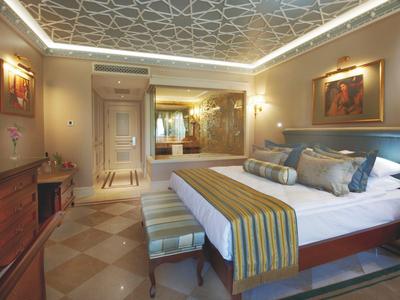 Weißes Hotelgebäude mit Balkonen und roten Dachziegeln umgeben von grünen Bäumen.