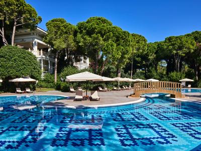 Schwimmbad mit blauen Mosaiken, Liegestühlen und Sonnenschirmen in einem Hotelgarten bei klarem Himmel