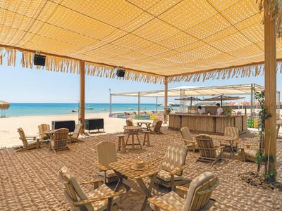 Offener Strandbereich mit Sitzgelegenheiten und Bar unter einem großen Sonnensegel.