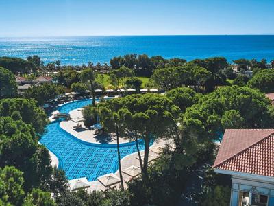Poolanlage mit Schwimmbecken, umgeben von Bäumen und Blick auf das Meer