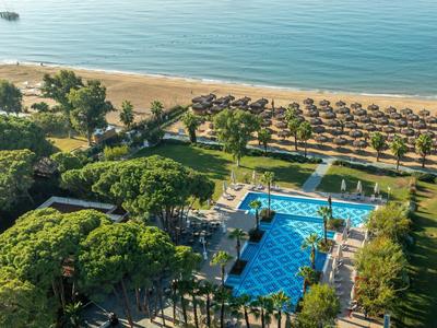 Piscine d'hôtel entourée d'arbres avec vue sur la plage et la mer en arrière-plan.