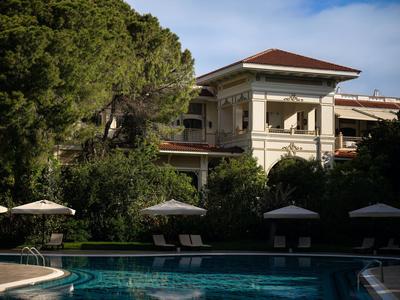 Bâtiment d'hôtel avec piscine, arbres et parasols par une journée ensoleillée.