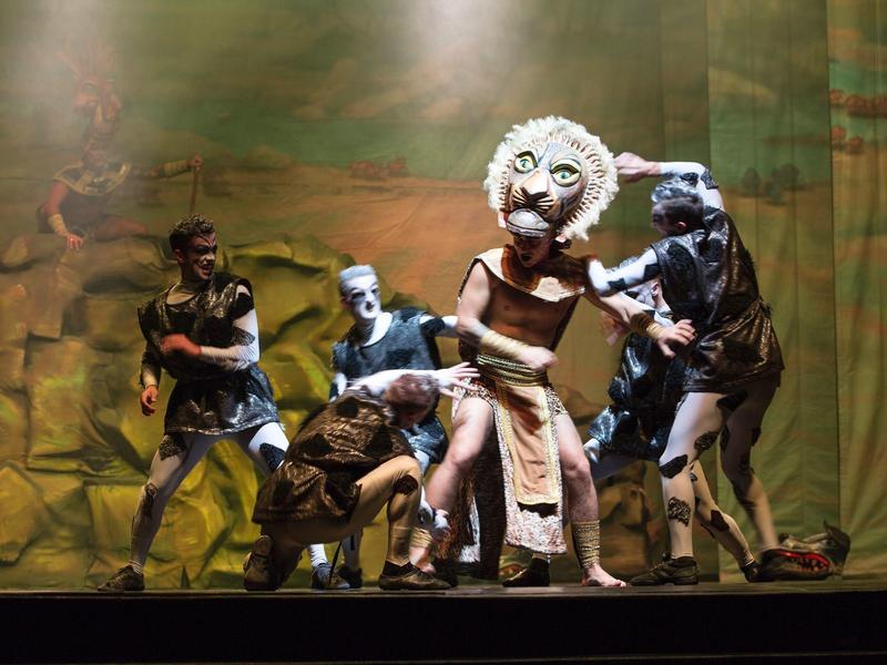 Theaterszene mit Darstellern in fantasievollen Kostümen vor einer gemalten Kulisse