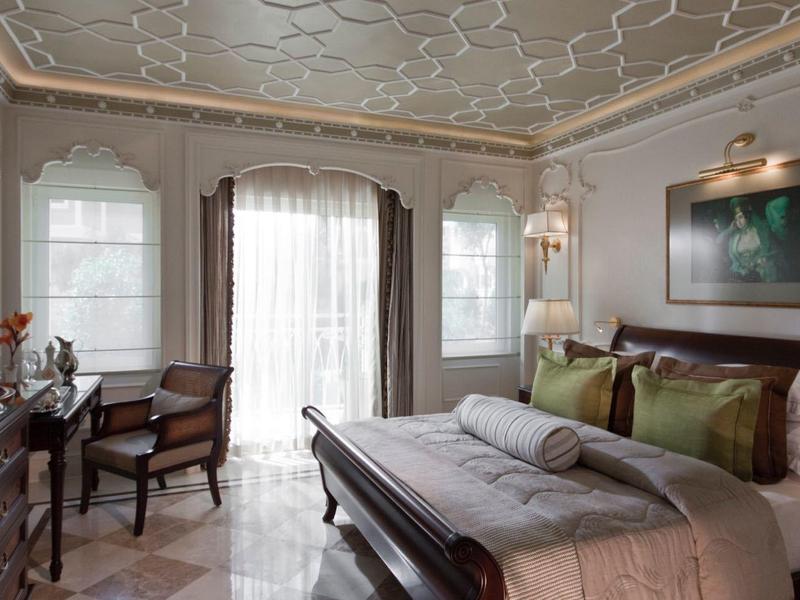 Elegantes Schlafzimmer mit Doppelbett, Schreibtisch, Stühlen und großen Fenstern mit Vorhängen.