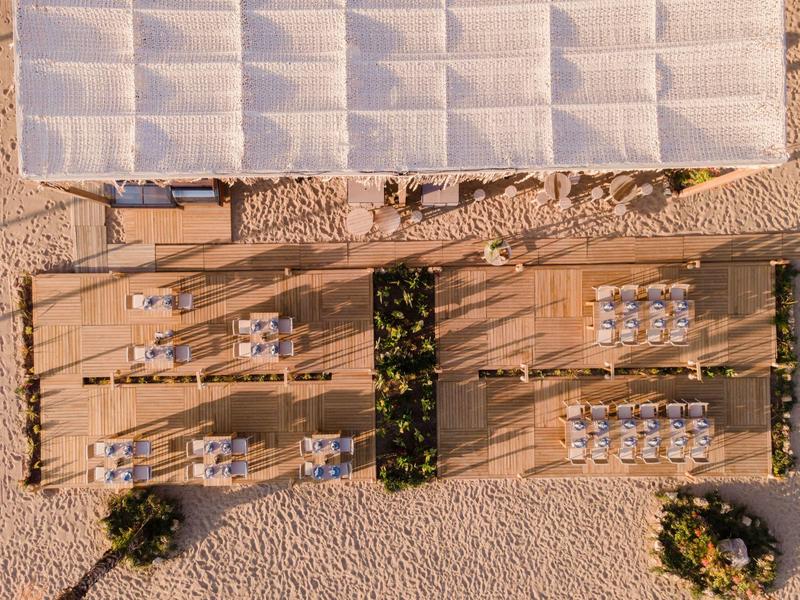 Vogelperspektive eines Strandrestaurants mit Holzstegen und Sitzbereichen auf Sandboden.