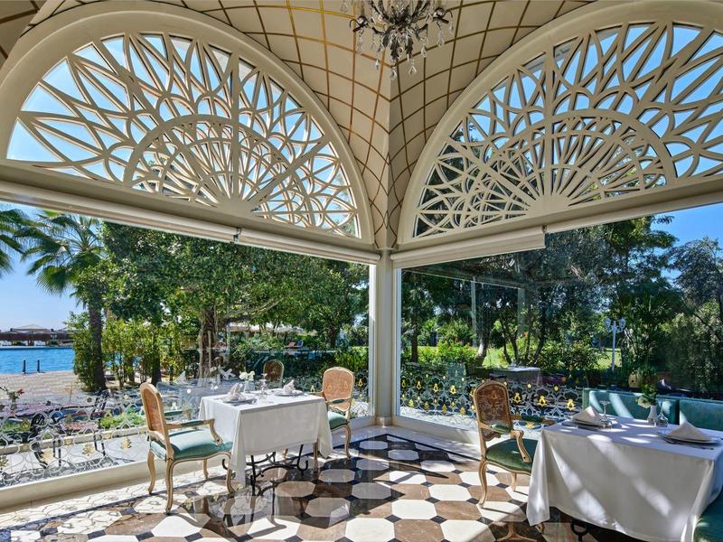 Offener Pavillon mit Tischen und Stühlen, Blick auf Garten und Wasser unter blauem Himmel.