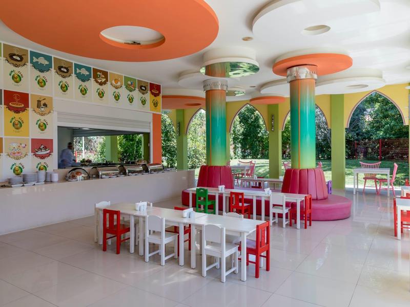 Bunter Kinderspielraum mit kleinen Tischen und Stühlen in einem lichtdurchfluteten Bereich.