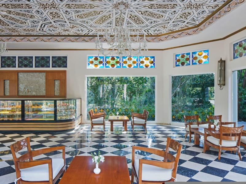 Helle Hotellobby mit gefliesten Böden, dekorativer Decke und Sitzgelegenheiten mit Gartenblick.