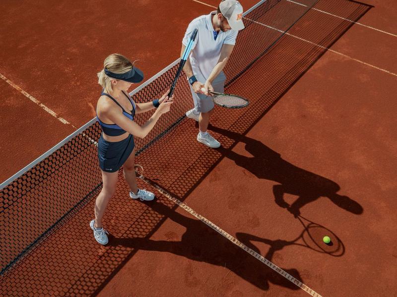 Zwei Personen stehen auf einem Tennisplatz neben dem Netz und halten Tennisbälle.
