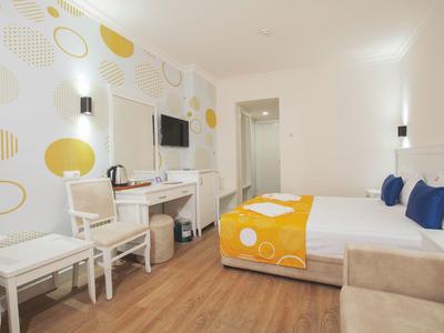 Modernes Hotelzimmer mit Doppelbett, gelben Akzenten, zwei Stühlen und Holzboden.