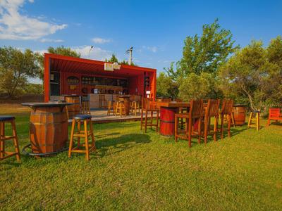 Rote Outdoor-Bar mit Holzstühlen und Tischen auf grünem Rasen bei sonnigem Himmel.