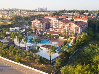 Ferienanlage mit Hotels, Pool, Palmen und viel Grün an einer Straße in hügeliger Landschaft.