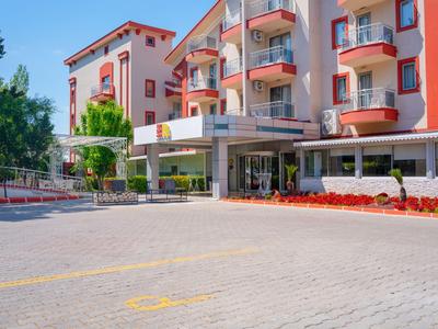 Wielopiętrowy hotel z balkonami, otoczony drzewami i kwiatami, pod czystym niebem.