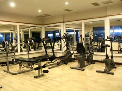 Fitnessraum mit großen Spiegelwänden, Laufbändern, Ergometern und hellem Holzboden.