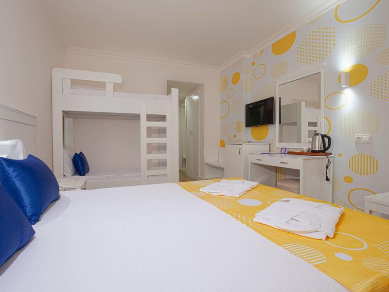 Pokój hotelowy z łóżkiem piętrowym, łóżkiem podwójnym z żółtą pościelą i niebieskimi poduszkami.