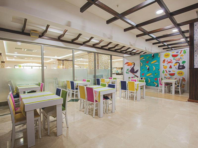 Jasna, nowoczesna restauracja z kolorowymi krzesłami i dekoracjami na ścianach.