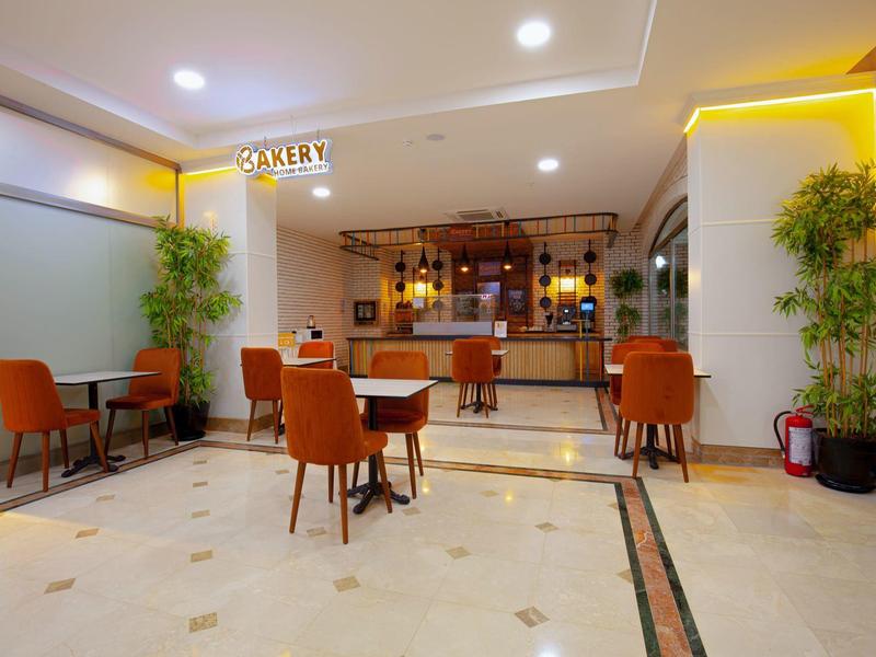 Nowoczesna strefa wypoczynkowa hotelu z pomarańczowymi krzesłami, stolikami i podświetlanym barem.