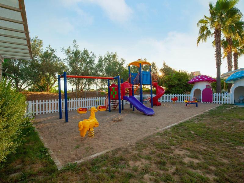 Kolorowy plac zabaw z zjeżdżalniami i huśtawkami obok palm w ośrodku wakacyjnym.