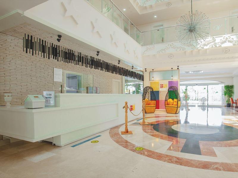 Jasne lobby hotelowe z recepcją, miejscami do siedzenia i kolorowymi dekoracjami.