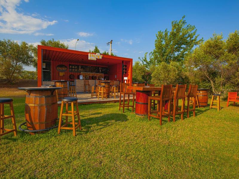 Bar na świeżym powietrzu z drewnianymi stołkami i stolikami na zielonej trawie pod niebieskim niebem.