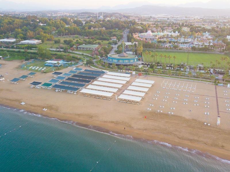 Widok z lotu ptaka na plażę z leżakami, basenami i zielonymi terenami obok hoteli.
