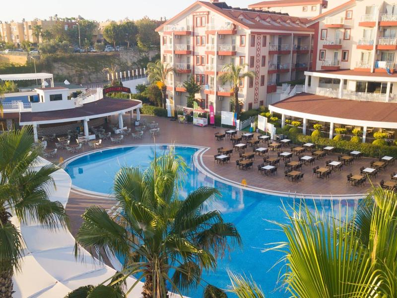 Ośrodek hotelowy z dużym basenem, leżakami i palmami w świetle słonecznym.