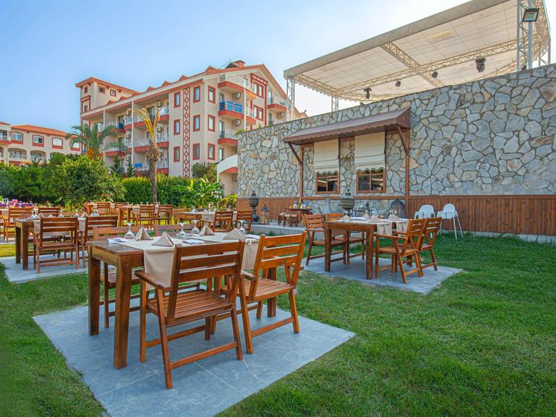 Strefa zewnętrzna hotelu z drewnianymi stołami i krzesłami na trawie pod czystym niebem.