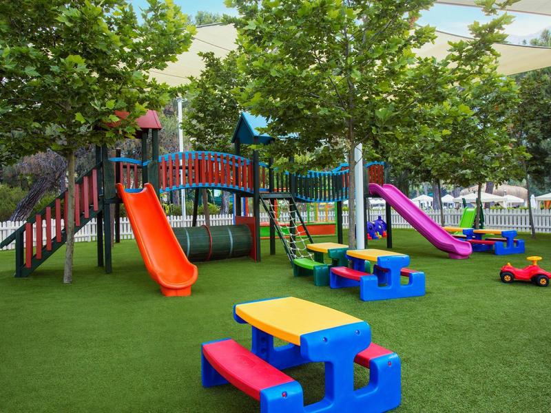 Colorful playground with slides, climbing equipment, and picnic tables on green artificial turf.