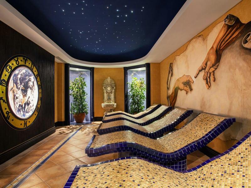 A luxurious spa room with heated curved loungers, plants, and decorative wall art.
