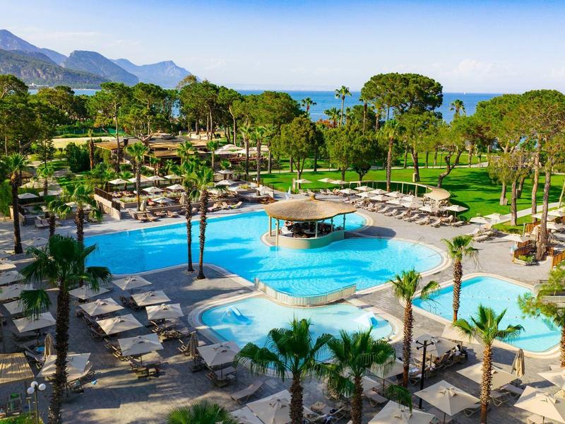 Hotel pool area with sun loungers, palm trees, and sea and mountain views.
