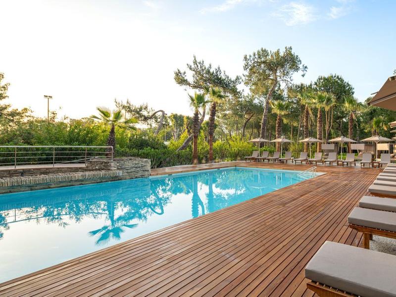 Modern pool area with wooden deck and lounge chairs in a green setting.