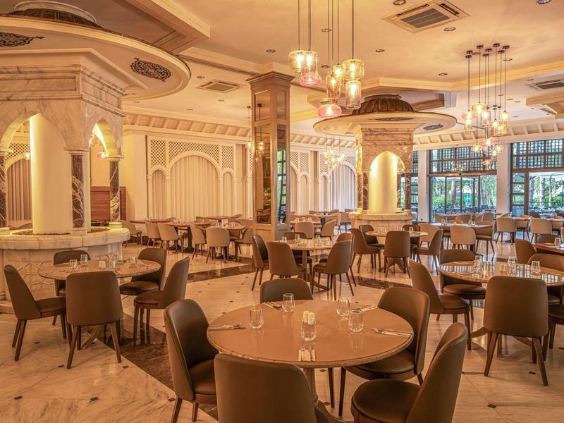 Elegant hotel restaurant with round tables and modern chairs in warm lighting.