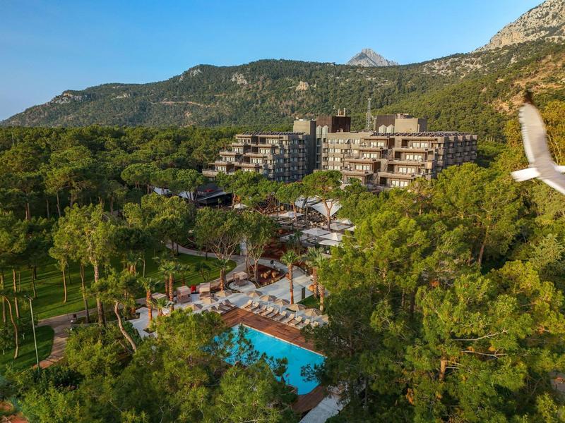 Hotel complex with pool surrounded by trees and mountains in the background