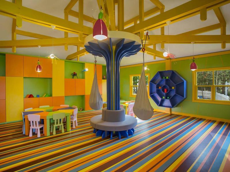 Colorful children's playroom with striped floor, benches, climbing structures, and bright ceiling in hotel.