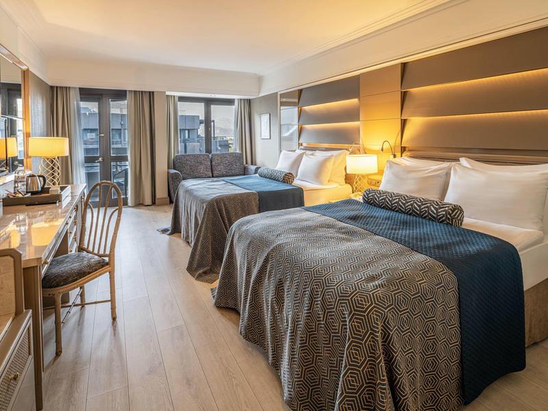 Modern hotel room with two double beds, desk, and large window overlooking outside.