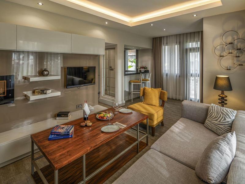 Modern living room with gray sofa, yellow armchair, and wooden table in a hotel room.