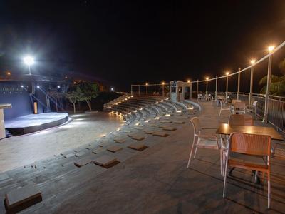 Terraza nocturna con mesas y asientos junto a un acogedor jacuzzi.
