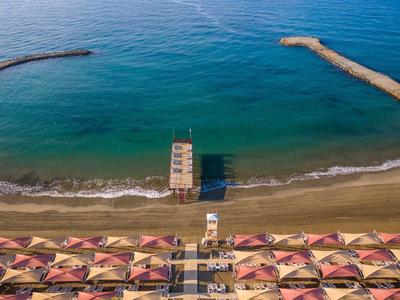 Aerial view of a beach with umbrellas, a lifeguard tower, and breakwaters in the sea.