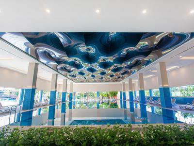Modern indoor pool with glass walls and artistically designed blue ceiling in a hotel.