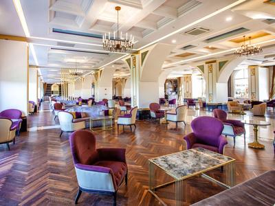 Bright, spacious hotel lounge with elegant armchairs, marble tables, and chandeliers.