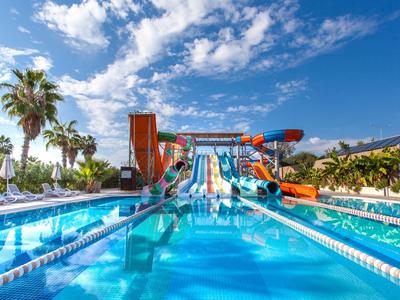 Bright outdoor pool with colorful water slides and palm trees under blue sky.