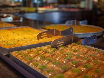 Close-up of trays with different desserts, including baklava, in a restaurant.