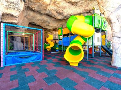 Colorful playground with slides and trampoline inside a rock cave at a hotel.
