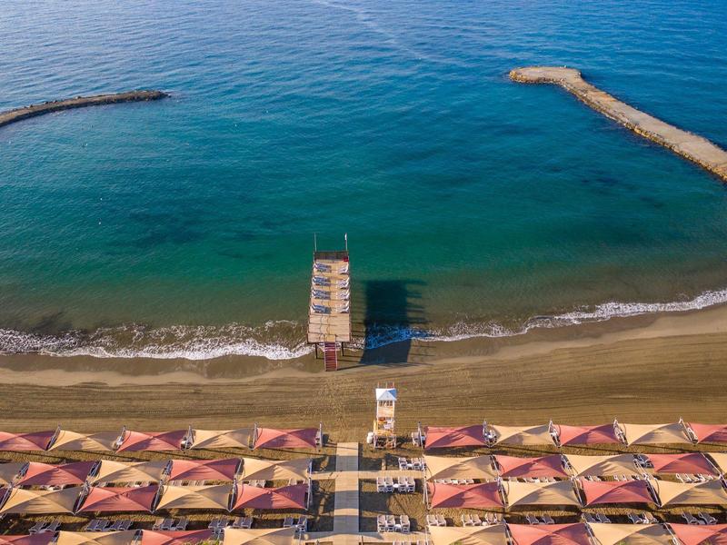 Aerial view of a beach with umbrellas, a lifeguard tower, and breakwaters in the sea.