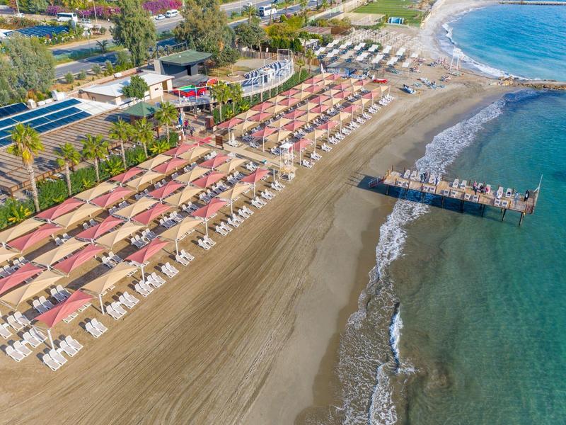 Long sandy beach with sun umbrellas and lounge chairs beside clear blue sea and pier.