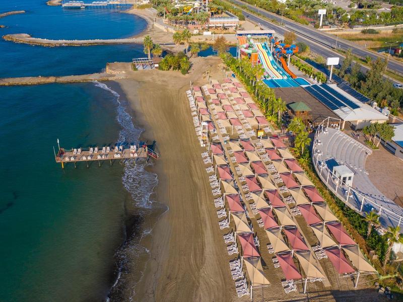 Aerial view of a beach with umbrellas, loungers, and water slides next to a hotel.