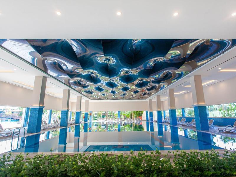 Modern indoor pool with glass walls and artistically designed blue ceiling in a hotel.