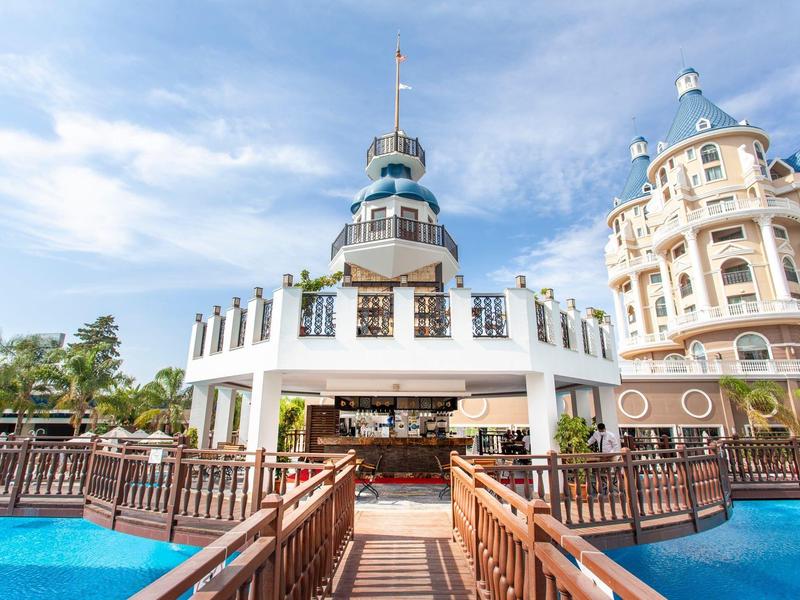 An elegant hotel building with a round tower top and adjoining wooden walkways over blue water.