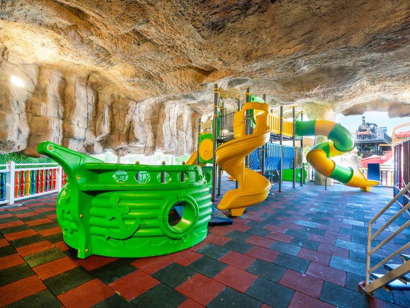 Colorful children's play area with slides and pirate ship inside a cave.