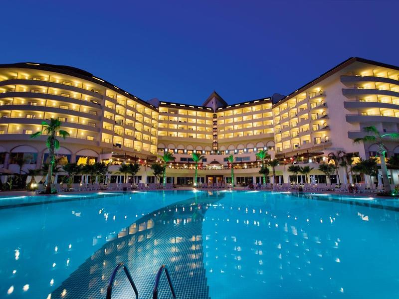 Oświetlony budynek hotelu z dużym basenem w nocy pod czystym niebem.